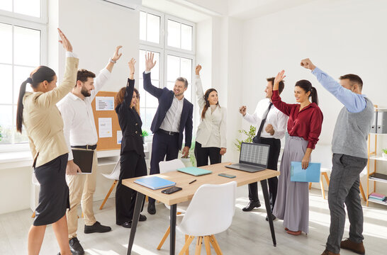 Business team celebrating success during a meeting in the office by raising hands together. People conveys teamwork, collaboration, and shared achievements in a professional setting.