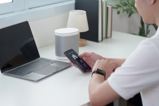 Smart Technology. A man using smartphone with smart speaker on desk.