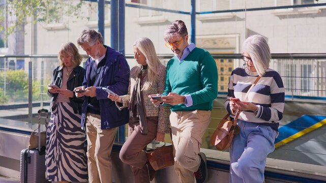 Stylish senior friends using smartphones together outdoors