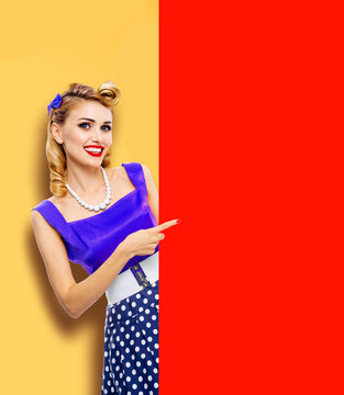 Beautiful smile woman in pinup blue dress point red blank banner with mockup free text space. Pin up girl advertise, isolated orange yellow background. Blond model in retro vintage sales ad concept
