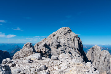 The jagged limestone summit of Jof di Montasio rises dramatically against a deep blue sky. Rugged peak in the Julian Alps showcases the raw beauty of the Italian mountains, challenging hikers to climb