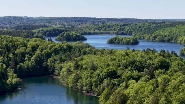 Aerial footage featuring a lush green forest surrounding a winding lake or series of connected ponds, with clear blue water and gently curving shorelines.