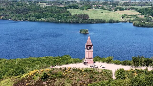 Aerial footage of the Himmelbjerget tower rising above the landscape, with a blue lake and green woodlands in the background.