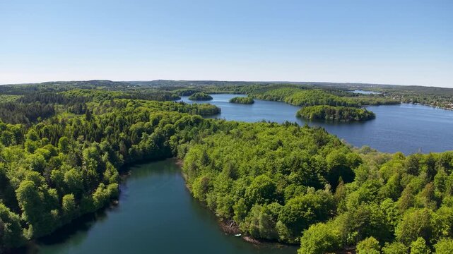 Drone footage of a tranquil lake dotted with small forested islands and surrounded by lush green trees and clear blue water.