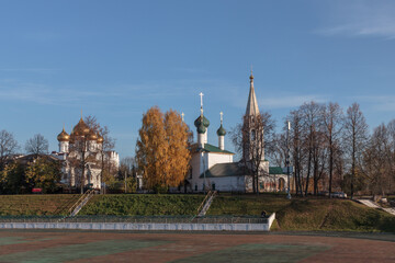 Historic churches in Yaroslavl under blue sky with autumn trees and green lawn.
