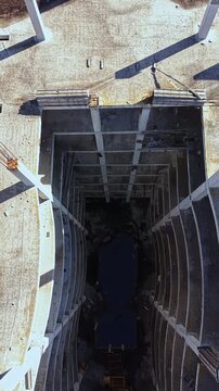 Aerial view showcases a deep void in a derelict building site with stark lines and shadows creating a haunting ambiance. The remnants of construction lay scattered below.