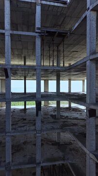 The view reveals the skeletal remains of a concrete building, featuring multiple levels with columns and open spaces. Sunlight filters through, highlighting the raw materials.