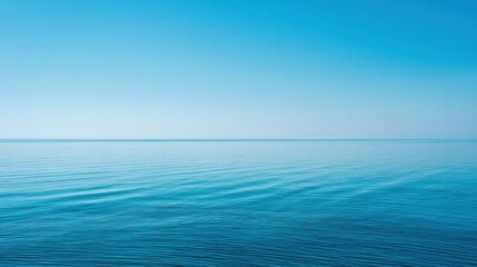 Obraz premium Calm blue ocean stretches toward the horizon blending with a clear bright sky. Gentle waves create a serene atmosphere reflecting sunlight on the water's surface.
