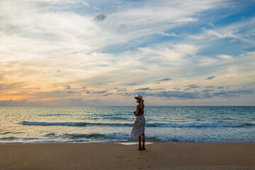 A pensive young woman in autumn clothes strolls along the beach at sunset, looking at the ocean waves. A romantic mood.