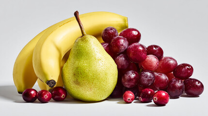 A still life of bananas, a pear, red grapes, and cranberries on white.