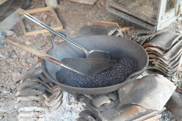 Traditional roasting process of black beans in an iron pan over a wood-fired stove