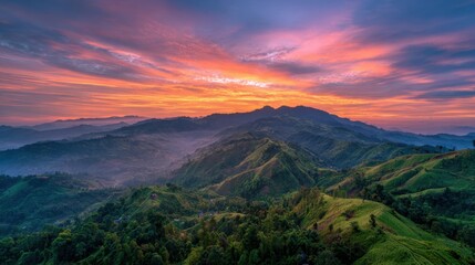 Fototapeta premium A breathtaking sunrise paints the sky with vibrant colors above rolling green hills and valleys. Soft mist lingers in the valleys creating a serene atmosphere at dawn.