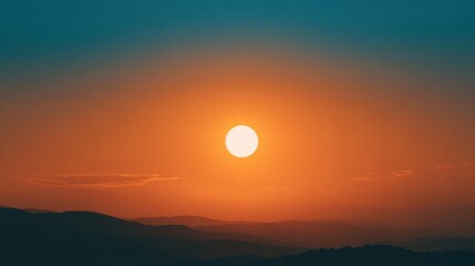 A bright sun sets behind distant mountains casting orange and blue hues across the sky. This breathtaking scene captures the beauty of nature at dusk providing a peaceful moment.