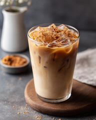Iced tahini latte in a clear glass filled with ice cubes, topped with a sprinkle of brown powder.