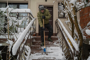 dorosła osoba odśnieża schody przy budynku