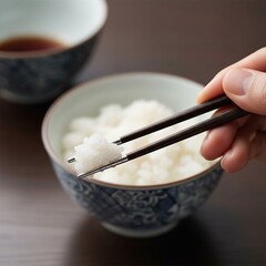 Hand using traditional wooden chopsticks to pick up fluffy white steamed rice from patterned bowl.