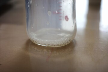 Close-up of Bubbles and Remaining Milk in an Empty Baby Bottle on a Wooden Table