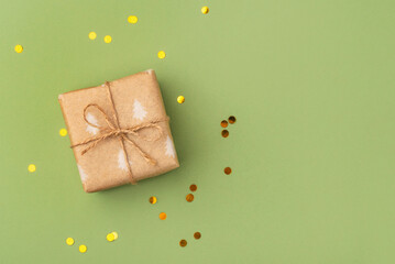 A Christmas gift wrapped in eco-friendly packaging on a green background with golden confetti