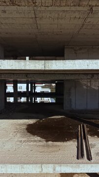 Sunlight floods an unfinished building, illuminating bare concrete walls and floors. Heavy beams and dirt are scattered around, highlighting ongoing construction and urban transformation.