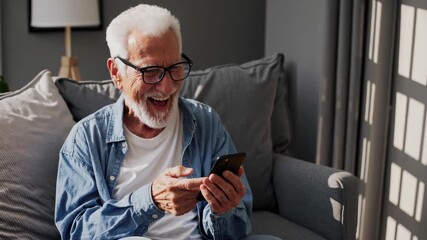 Senior man using smartphone with smile. Laughter and happiness on sofa during video call. Casual home shows communication and technology use. Relaxed friendly atmosphere of senior lifestyle wellbeing. - Powered by Adobe