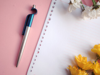 Top view of empty notepad and spring flowers on pink desk.

