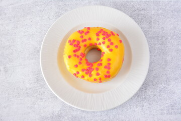 a top view of Bright Yellow Donut with Red Heart Sprinkles on a White Plate
