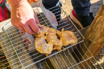 A person prepares marinated chicken on a grill rack during an outdoor camping and hiking trip.