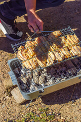 Chicken cooks on a portable grill by a lake during a hiking and outdoor travel stop. 