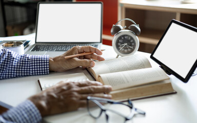 close up shot, asian man open book to study and working online with tablet and laptop on desk, Increasing knowledge concept