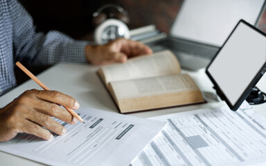 asian man checking business document find knowledge in book using tablet and laptop to working online via internet technology, close up shot