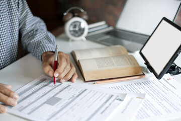 asian man checking business document find knowledge in book using tablet and laptop to working online via internet technology, close up shot