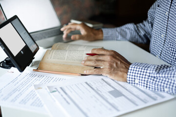 asian man reading book using tablet and laptop with documents working and learning online to Increasing knowledge via internet technology, close up shot