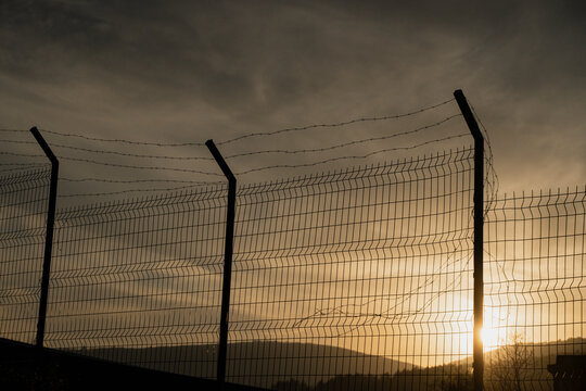 Border Fence at Sunset. Migration and Political Tension Concept - Powered by Adobe