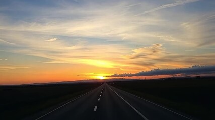POV driving on a straight highway towards a vibrant sunset. Traveling down an empty country road at dusk. Road trip and journey concept