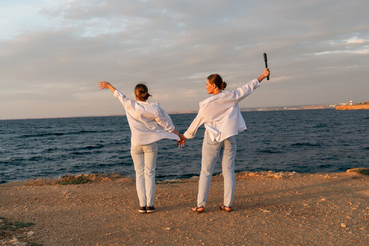Couple Beach Sunset Holding Hands - Two people in white shirts stand on a beach holding hands with the sunset in the background.