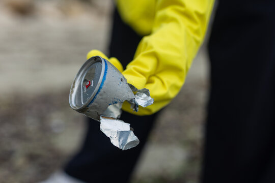 volunteer picking up a crushed metal can during beach cleanup, highlighting pollution, waste problem, ecology, coastal protection and environmental awareness.
