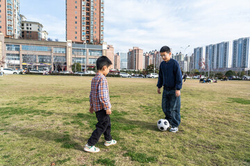 A father and a son are playing football on a grassy open area, enjoying a pleasant outdoor activity.