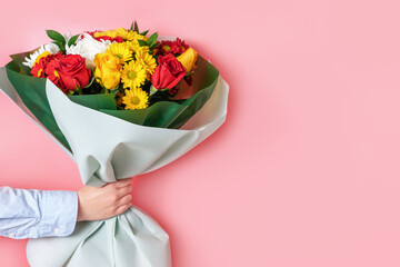 emale hand holds a bouquet of flowers on pink background close-up.