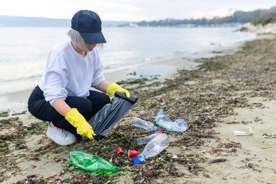 volunteer collecting plastic bottles on a polluted beach, highlighting ocean pollution, waste problem, environmental protection and coastal cleanup action. - Powered by Adobe
