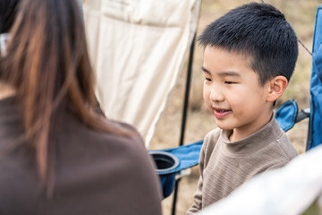 A young boy is smiling while interacting with an adult in an outdoor setting, likely during a camping activity.