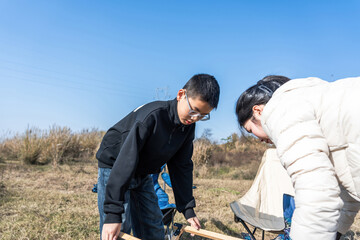 Two individuals are collaborating on a task in an outdoor grassy area under a clear sky.
