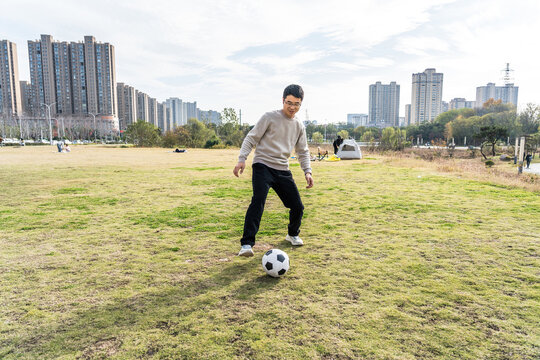 A young man is engaged in playing soccer on a grassy field within an urban park setting. - Powered by Adobe