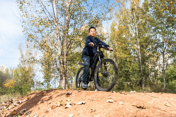Naklejka premium A young boy is seen riding a bicycle in a picturesque outdoor park surrounded by trees and autumn foliage.