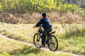 Obraz premium A boy is riding a bicycle on a grassy path surrounded by nature, enjoying an outdoor leisure activity.