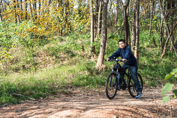 Fototapeta premium A man is cycling on a dirt path in a forest filled with green plants and trees.