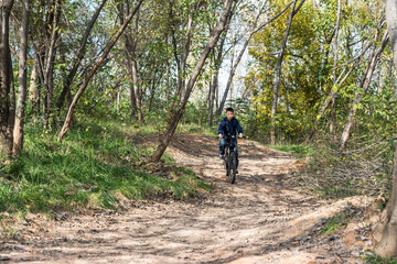 Naklejka premium A person is cycling on a dirt path surrounded by trees and greenery in an outdoor wooded area.