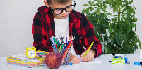 Child writing or drawing at a desk surrounded by school supplies, books, an apple,and an alarm clock