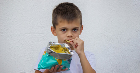 Close-up of a happy little boy enjoying and eating potato chips directly from the snack bag.