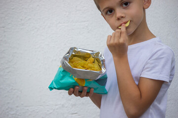 Close-up of a happy little boy enjoying and eating potato chips directly from the snack bag.
