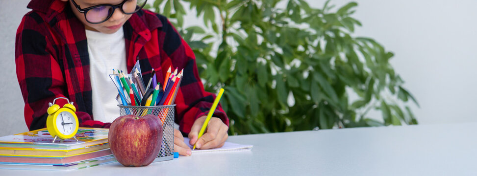 Child writing or drawing at a desk surrounded by school supplies, books, an apple,and an alarm clock - Powered by Adobe